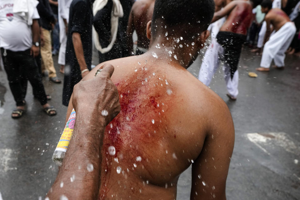 A man sprays rose water on a Shiite Muslim's lacerations after the latter had flagellated himself during a procession to mark Ashoura in Kolkata, India, Saturday, July 29, 2023. Ashoura is the tenth day of Muharram, the first month of the Islamic calendar, observed around the world in remembrance of the martyrdom of Imam Hussein, the grandson of Prophet Mohammed. (AP Photo/Bikas Das)