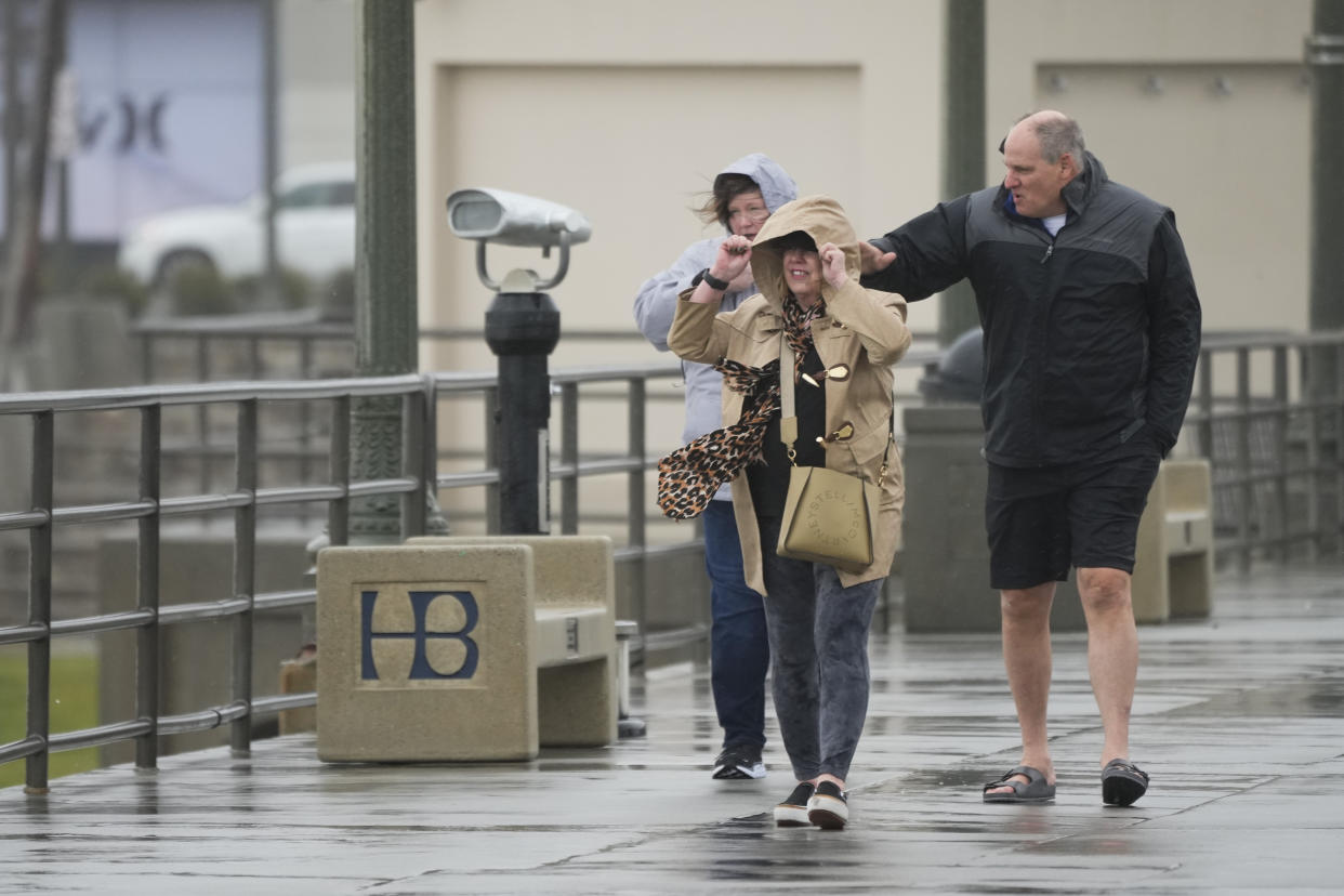 People walk along the Huntington Beach Pier on Friday, Feb. 24, 2023, in Huntington Beach, Calif. California and other parts of the West faced heavy snow and rain Friday from the latest winter storm to pound the U.S. (AP Photo/Ashley Landis)