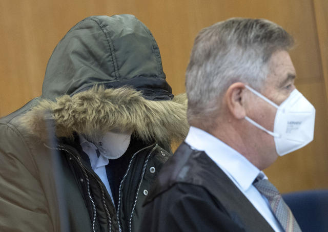 An unidentified Syrian doctor sits in the security room of the Higher Regional Court with one of his lawyers Ulrich Endres at right, in Frankfurt, Germany, Wednesday, Jan. 19, 2022. A court in Germany will begin hearing a case against a Syrian doctor accused of crimes against humanity for torturing and killing inmates at a government-run prison in his home country. Federal prosecutors say the doctor worked at a military intelligence prison in the Syrian city of Homs from April 2011 until late 2012. Prosecutors accuse him of killing one person and torture in 18 cases. (Boris Roessler/Pool Photo via AP)
