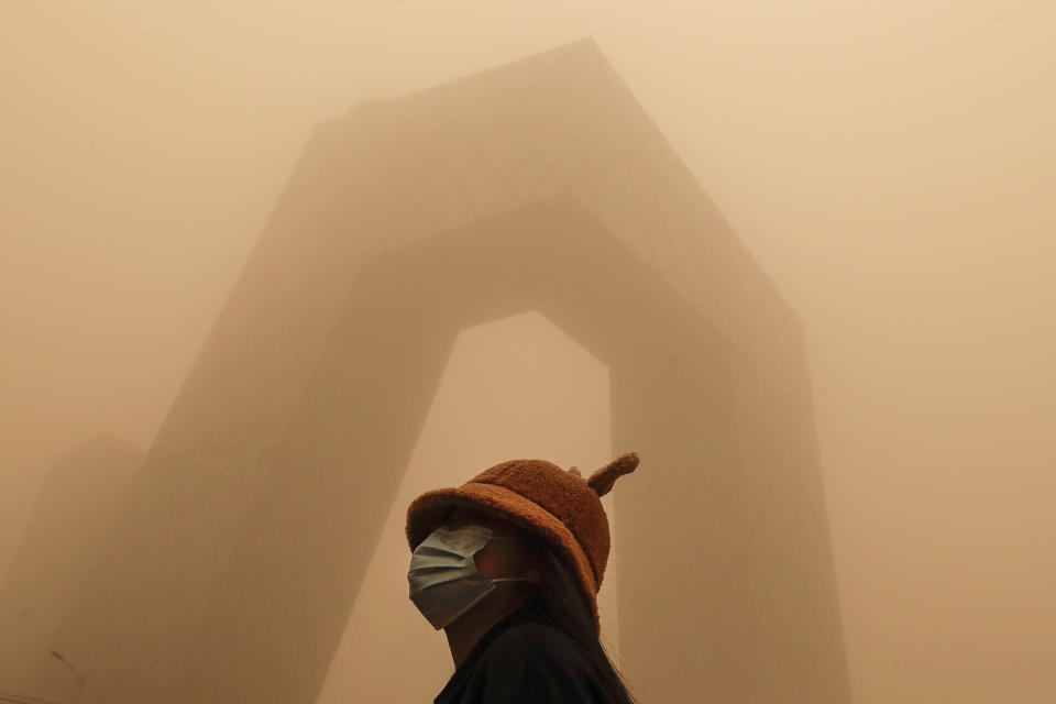 A woman wearing a face mask to help curb the spread of the coronavirus stands against the China Central Television (CCTV) building as capital city is hit by polluted air and a sandstorm in Beijing. (AP Photo/Andy Wong)