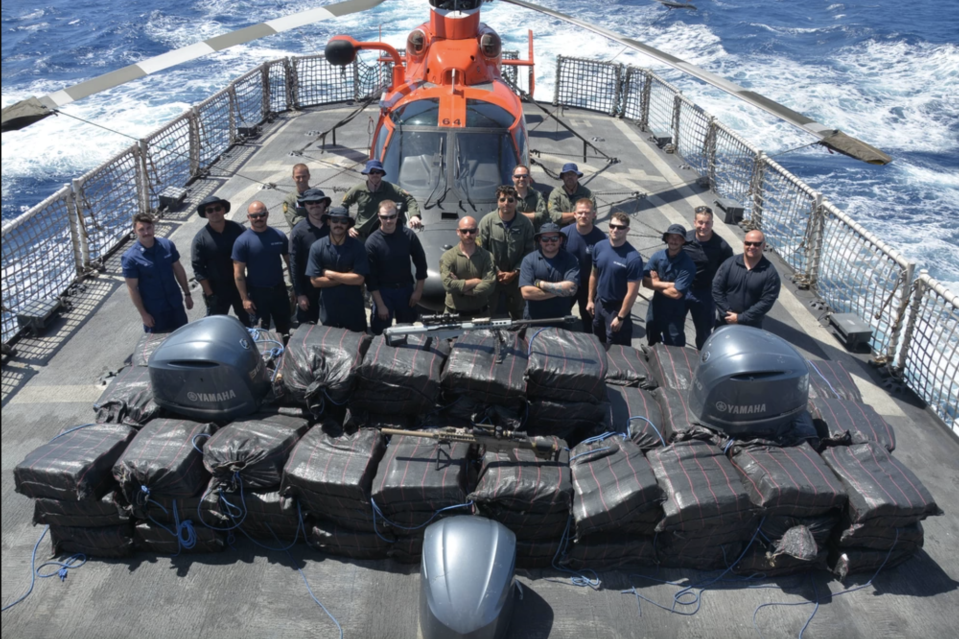 Crewmembers of the Coast Guard Cutter Alert (WMEC 630) stand behind cocaine bales seized from a drug smuggling vessel in Eastern Pacific waters. / Credit: Coast Guard