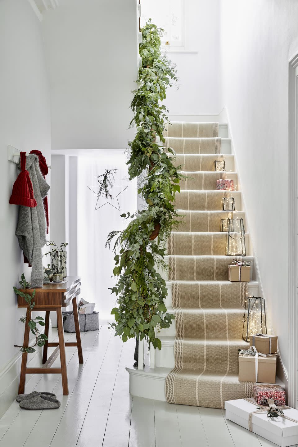 hallway, white wooden floors and stairway with fairy light filled lanterns runing up the stairs, green foliage along the banister