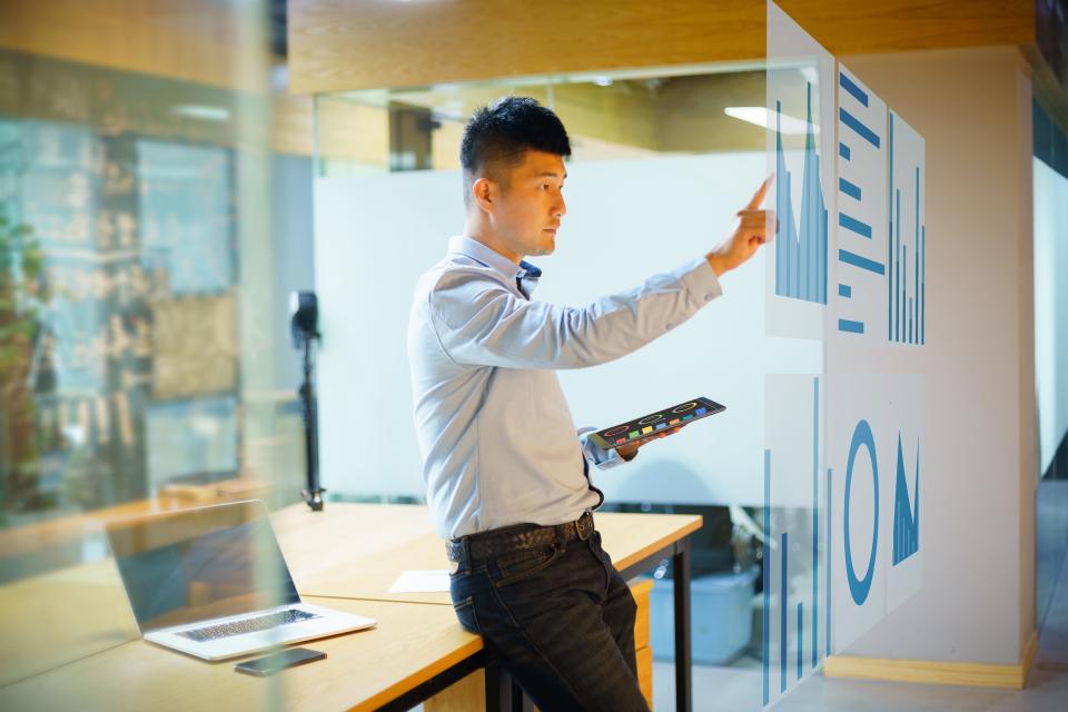 A man leaning up against a table in a meeting room while touching an AI-powered dashboard