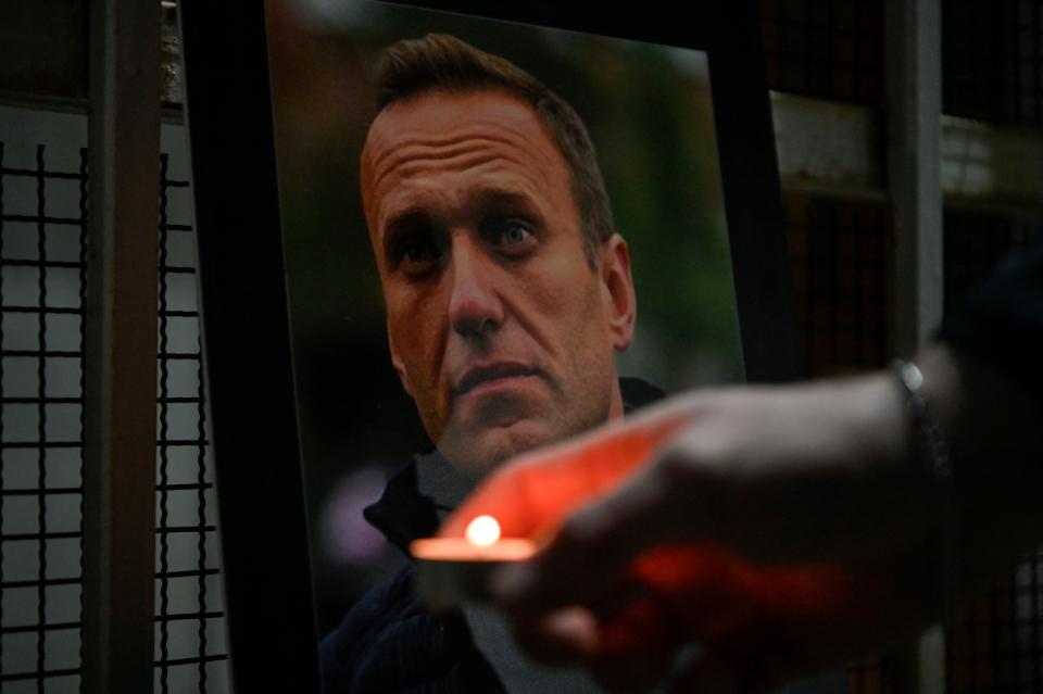 A person lights a candle by a portrait of late Russian opposition leader Alexei Navalny, who died in a Russian Arctic prison, placed at the entrance of the Chancery of the Embassy of the Russian Federation in Pristina on 20 February 2024 (AFP via Getty Images)