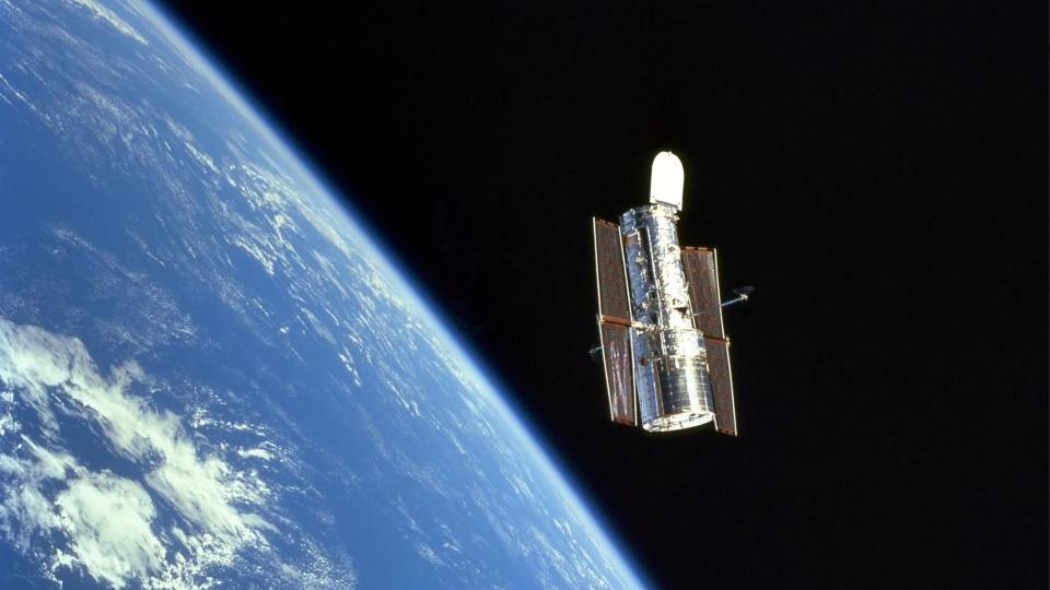 a cylindrical spacecraft floats above Earth