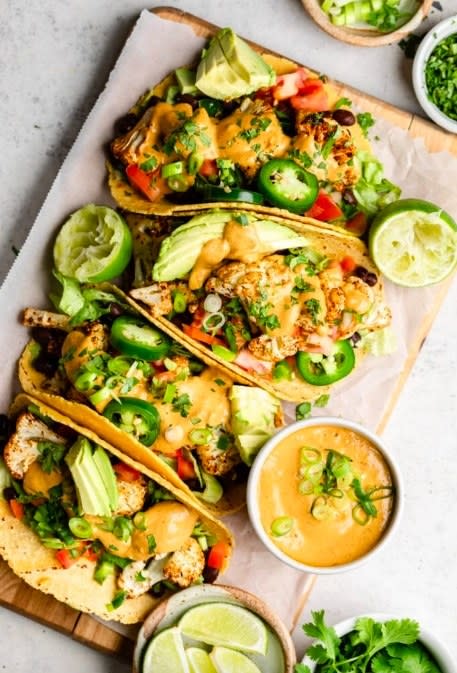 A row of cauliflower and black bean tacos stuffed to the brim with jalapeño slices, avocado slices, green onion slices, and topped with chipotle mayo.