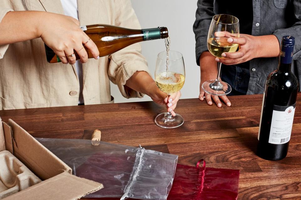 one person pouring a glass of wine while another person holds a full glass