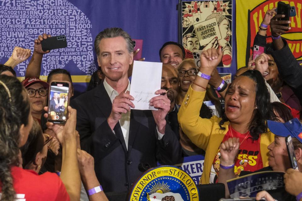 California Gov. Gavin Newsom, surrounded by fast-food workers, holding up a piece of legislation