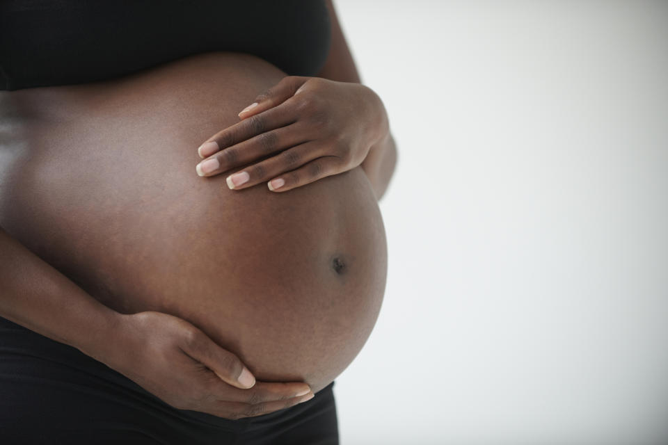 A close-up of a pregnant woman's belly with her hands gently resting on it. The woman is wearing a black top and pants