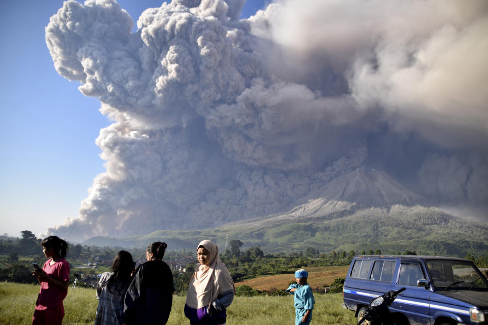 People watch as Mount Sinabung spews volcanic material during an eruption in Karo, North Sumatra, Indonesia, Tuesday, March 2, 2021. The 2,600-metre (8,530-feet) volcano erupted Tuesday, sending volcanic materials a few thousand meters into the sky and depositing ash on nearby villages. (AP Photo)