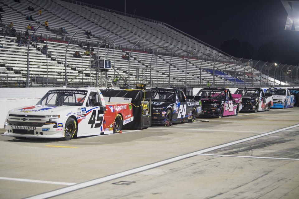 Trucks, with drivers not yet inside, line the track before the NASCAR Truck Series auto race at Martinsville Speedway in Martinsville, Va., Friday, Oct. 30, 2020, as some of the thousand fans allowed in sit in the stands. (AP Photo Lee Luther Jr.)