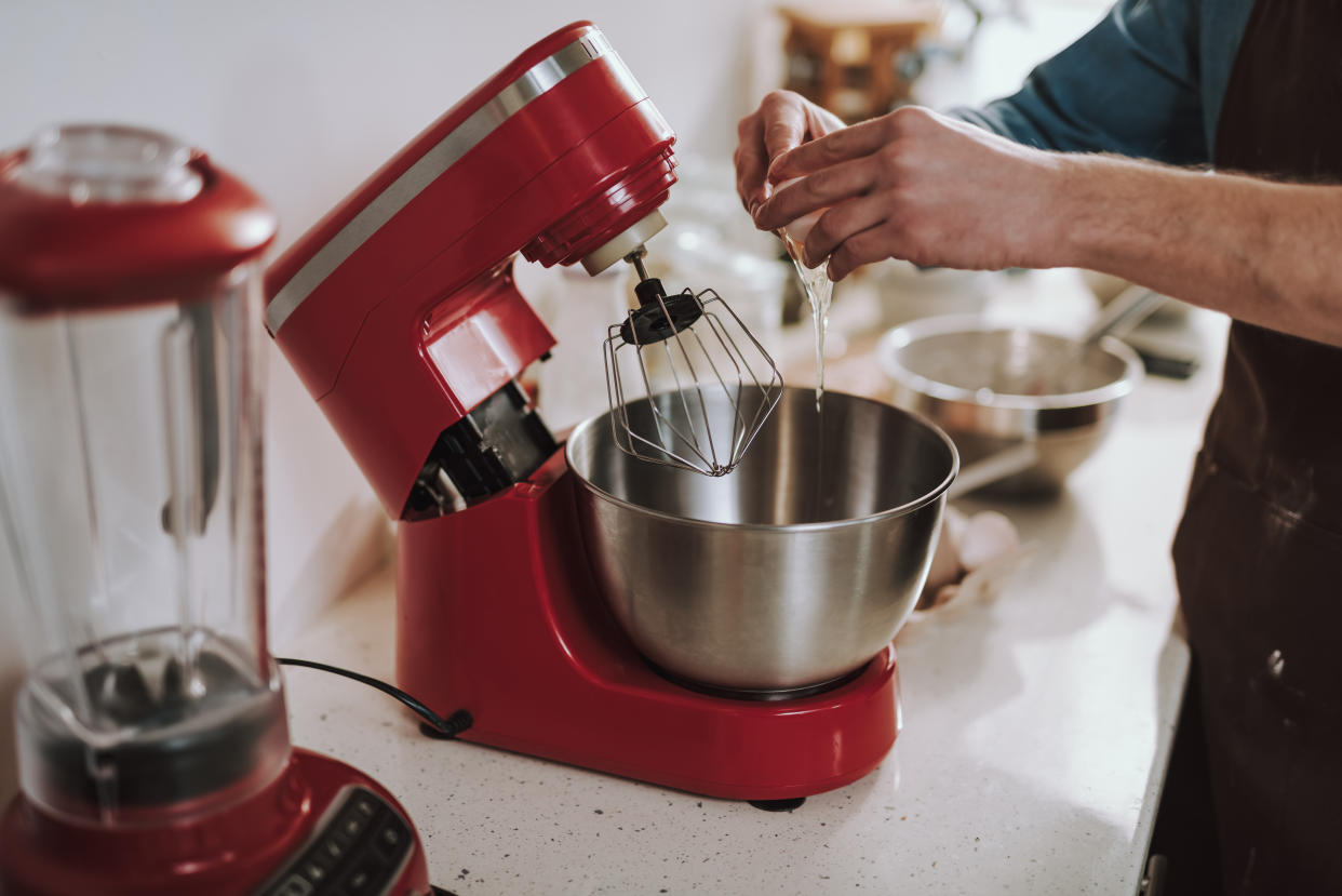 Modern red electric stand mixer with a big metal bowl and a man pouring raw egg into it
