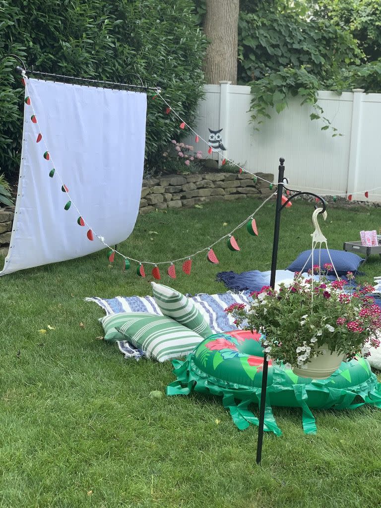 backyard movie night ideas diy movie screen, patio decorations, blankets, and pillows set up in the yard