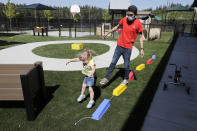 In this May 27, 2020 photo, Aaron Rainboth, a teacher at the Frederickson KinderCare daycare center in Tacoma, Wash., wears a mask as he takes part in a balance exercise with a child during an outdoor play period. In a world weary of the coronavirus, many working parents with young children are now struggling with the decision on when or how they'll be comfortable returning to their child care providers. Frederickson KinderCare, which has been open throughout the pandemic to care for children of essential workers, removed carpets and spaced out tables and chairs as part of their measures to control the spread of the coronavirus. (AP Photo/Ted S. Warren)
