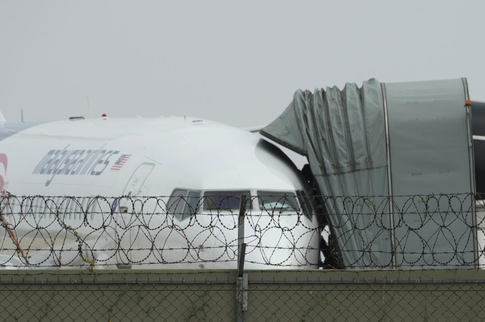 A Malaysian airplane is parked at Phnom Penh International Airport in Phnom Penh, Cambodia, Tuesday, April 11, 2023, before transporting Japanese citizens who were taken into custody on suspicion of running phone scam. Over a dozen of Japanese men detained in Cambodia in January on suspicion of taking part in phone and online scams were deported to their homeland on Tuesday, police said. (AP Photo/Heng Sinith)