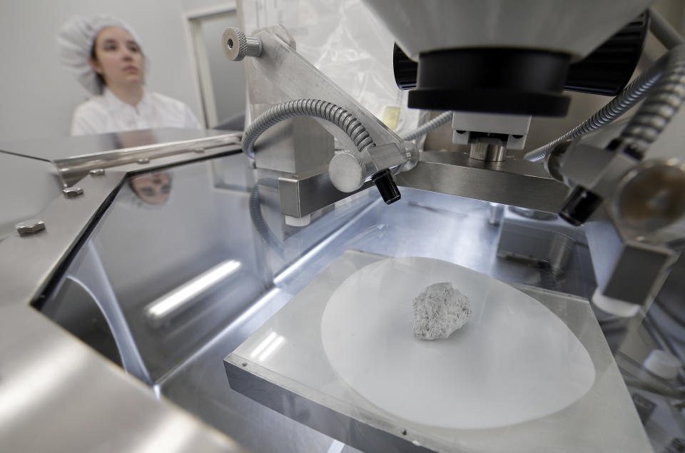 The Genesis Rock, foreground, a 4.4 billion year old anorthosite rock, approximately 2 inches in length, brought back by Apollo 15 and used to determine the moon was formed by a giant impact, sits under glass inside a pressurized nitrogen-filled examination case as Lacey Costello, an Apollo sample curation processor, works with other samples on the outside of the case inside the lunar lab at the NASA Johnson Space Center Monday, June 17, 2019, in Houston. (Photo: Michael Wyke/AP)