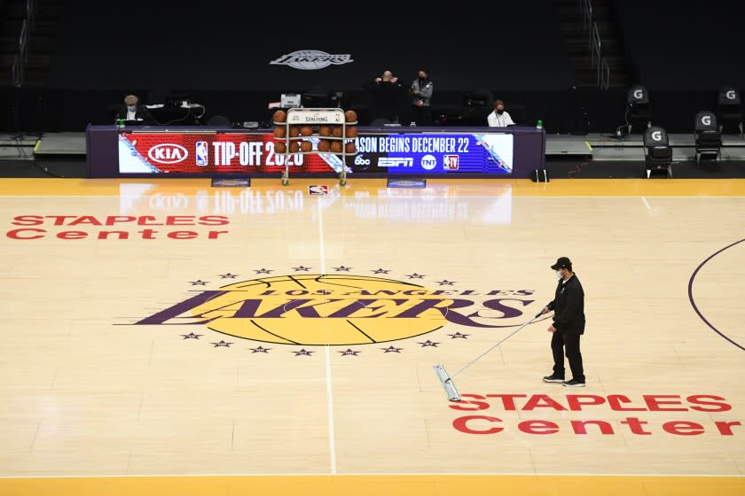 A Staples Center staff member with a mask on cleans the floor before an NBA preseason basketball game between the Los Angeles Clippers and the Los Angeles Lakers in Los Angeles, Sunday, Dec. 13, 2020. NBA hopes to kick off the regular season on Dec. 22, under pandemic. (AP Photo/Kyusung Gong)