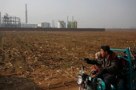 A villager and a boy ride on an electric tricylce past the Guantao Chemical Industry Park outside the village of East Luzhuang, Hebei province, February 23, 2017. Picture taken February 23, 2017. REUTERS/Thomas Peter