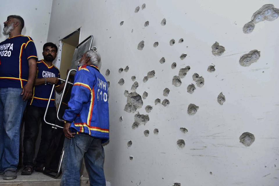 Rescue workers stand beside a bullet-riddled wall after security forces conducting operation against attackers at a police headquarters, in Karachi, Pakistan, Friday, Feb. 17, 2023. Militants launched a deadly suicide attack on the police headquarters of Pakistan's largest city on Friday, officials said, as the sound of gunfire and explosions rocked the heart of Karachi for several hours. (AP Photo/M. Noman)