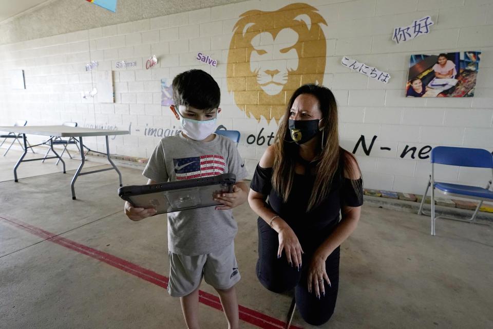 Lynette Faulkner, right, director at the Valencia Newcomer School, helps out new student Fernando Barron Escalante, 5, with his new iPad as he connects with classmates during remote learning, Tuesday, Sept. 2, 2020, in Phoenix. Communicating during the coronavirus pandemic has been trying for parents and students at the Phoenix school for refugees who speak a variety of languages and are learning to use technology like iPads and messaging apps. (AP Photo/Ross D. Franklin)