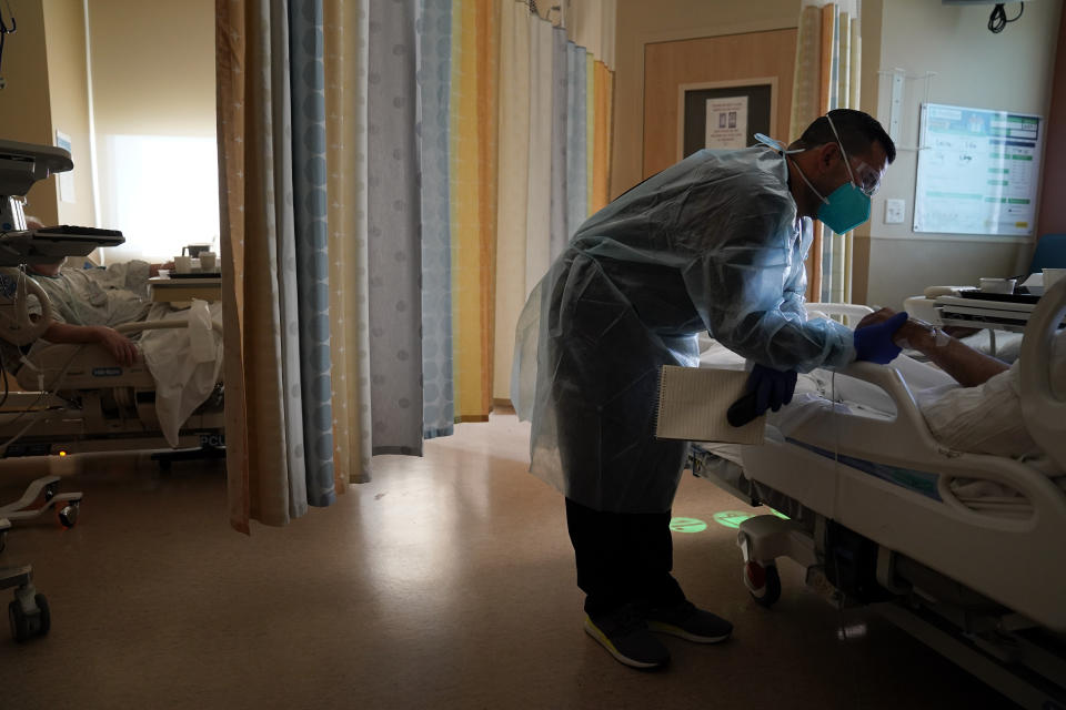 Chaplain Elias Mena holds the hand of a COVID-19 patient while praying for him at Providence Holy Cross Medical Center in the Mission Hills section of Los Angeles on Friday, Jan. 15, 2021. As families are barred from visiting loved ones to curb the disease's spread, chaplains often are there to act as surrogates, holding the hands of the dying, praying with them and carrying iPads into hospital rooms to provide a real-time connection with grieving families. (AP Photo/Jae C. Hong)