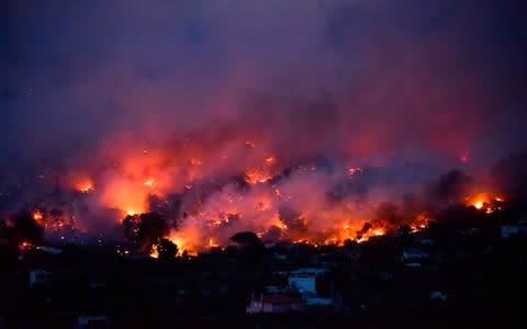 Flames rise as a wildfire burns in the town of Rafina, near Athens - Credit: AFP