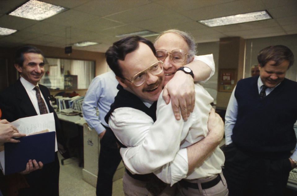 ARCHIVO - Terry Anderson, exrehén y corresponsal principal de The Associated Press para Oriente Medio, al centro a la izquierda, abraza a su colega Jim Abrams durante una visita el 12 de diciembre de 1991 a la oficina de la AP en Washington. (AP Foto/Greg Gibson, archivo)