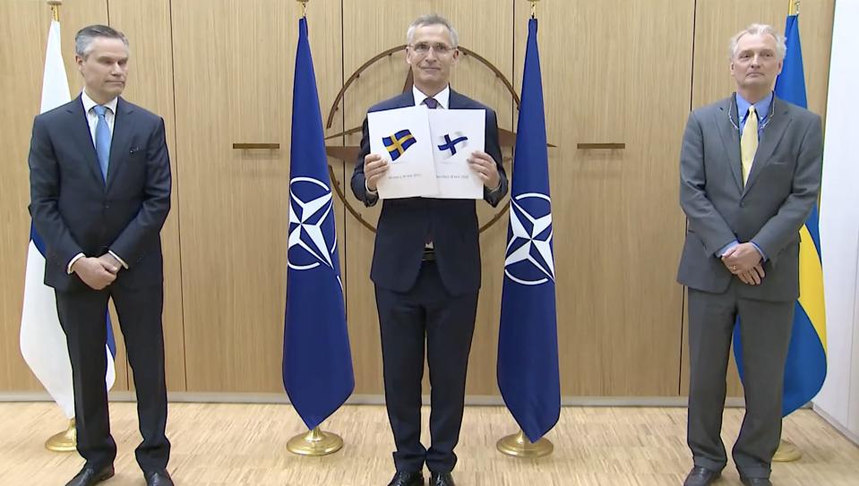 Jens Stoltenberg holding the flags of Sweden and Finland while posing for a picture with Klaus Korhonen and Axel Wenhoff.