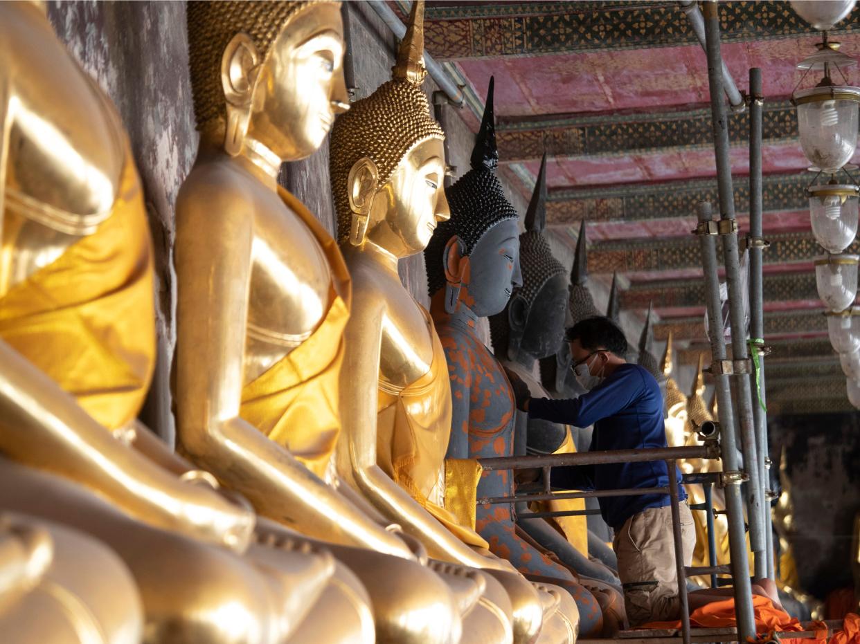 A Thai worker wears a face mask to protect from a new coronavirus as he repairs Buddha statues at Suthat Temple in Bangkok, Thailand, Tuesday, March 10, 2020.