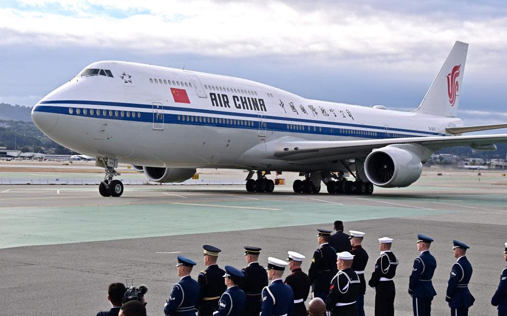 White jet on tarmac with people in uniform waiting in rows.