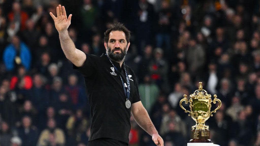 Sam Whitelock waves as he stands next to the Webb Ellis Cup trophy