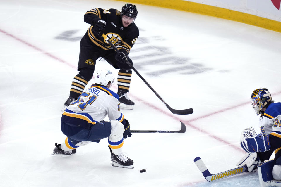 Boston Bruins center Jakub Lauko (94) centers the puck past St. Louis Blues defenseman Matthew Kessel during the first period of an NHL hockey game, Monday, March 11, 2024, in Boston. (AP Photo/Charles Krupa)