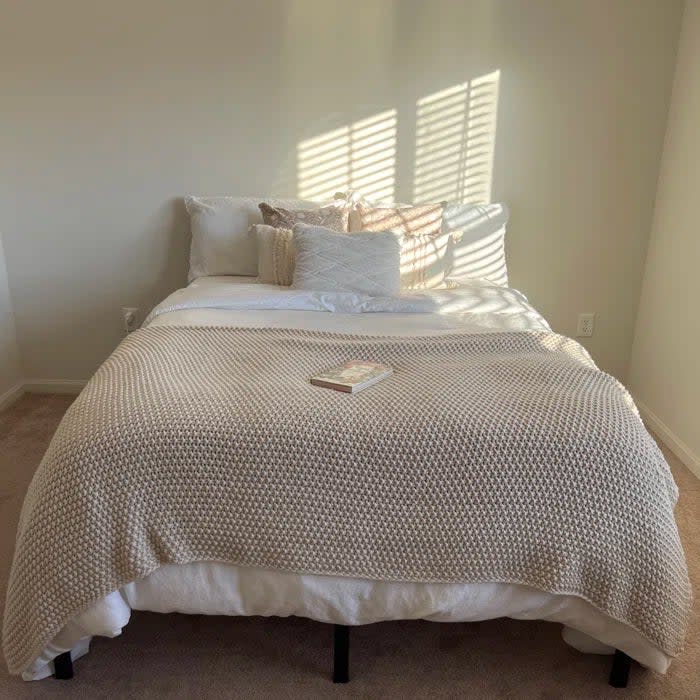 Reviewer's photo of the bed frame with a mattress, neatly made with textured bedding and a book placed on it, sunlight casting shadows on the wall