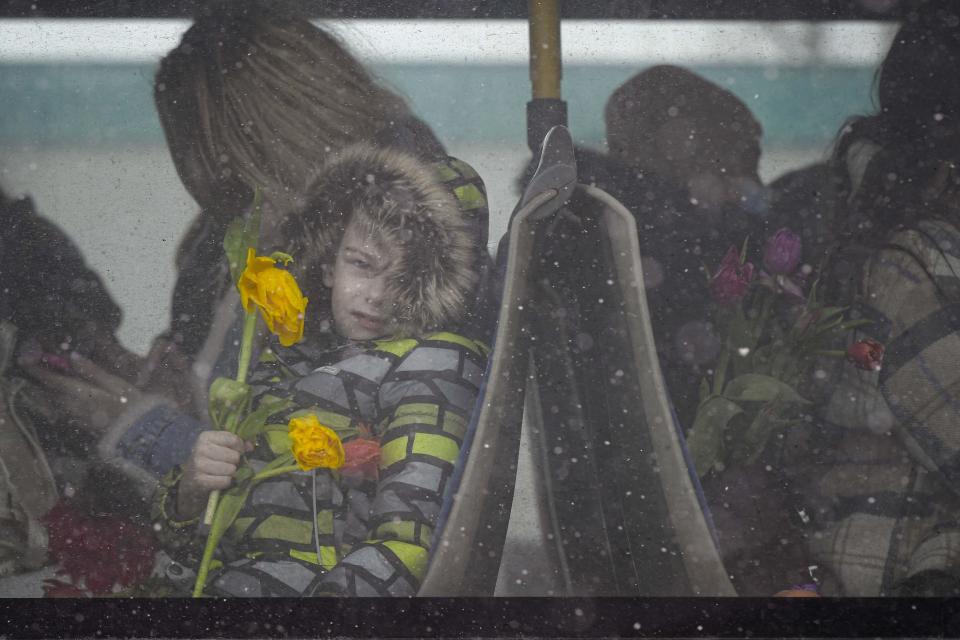 A refugee child fleeing the conflict from neighbouring Ukraine holds flowers, given out to celebrate International Women's Day, as he sits on a bus, at the Romanian-Ukrainian border, in Siret, Romania, Tuesday, March 8, 2022. It is a global day to celebrate women, but many fleeing Ukraine feel only the stress of finding a new life for their children as husbands, brothers and fathers stay behind to defend their country from Russia's invasion. (AP Photo/Andreea Alexandru)
