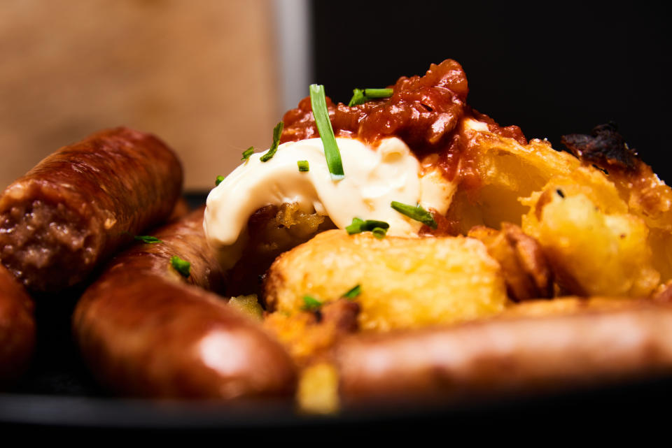 A plate of sausages, mashed potatoes with gravy, and garnish