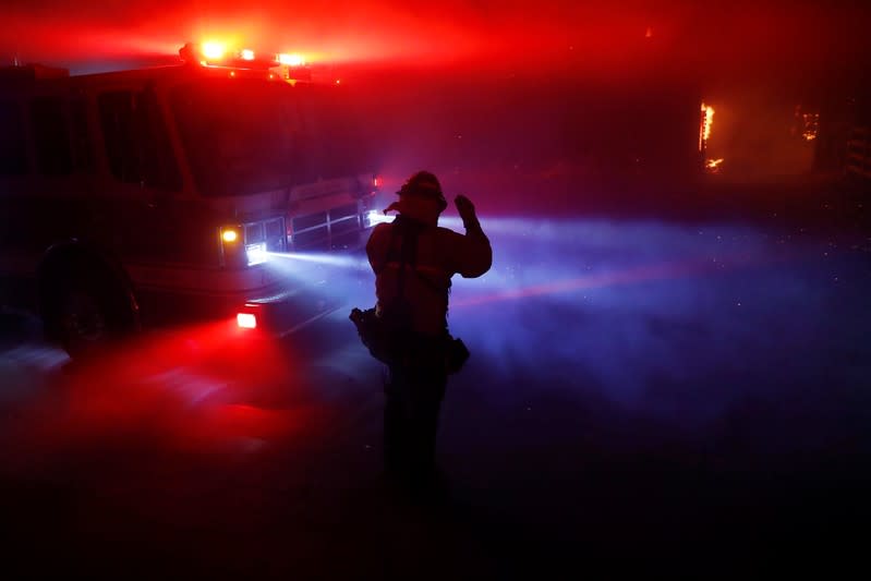 A firefighter walks through thick smoke illuminated by fire engine lights and embers during the wind-driven Kincade Fire in Windsor