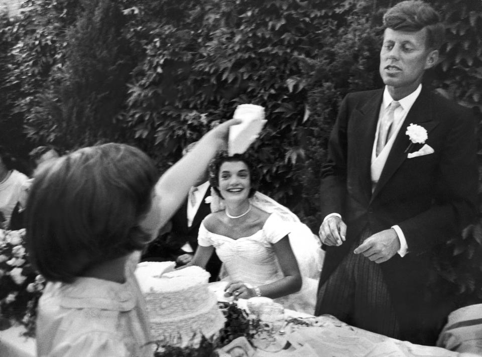 Flower girl Janet Auchincloss holding up a wedge of wedding cake for bridegroom Sen. John Kennedy as her half-sister bride Jacqueline Bouvier Kennedy looks on in amusement at table during formal luncheon at their wedding reception at her mother's estate. (Photo by Lisa Larsen/Time Life Pictures/Getty Images)