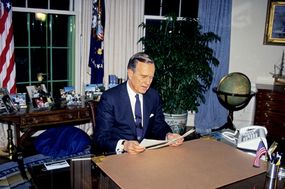 George H.W. Bush sits at a desk in the Oval Office, reading a document
