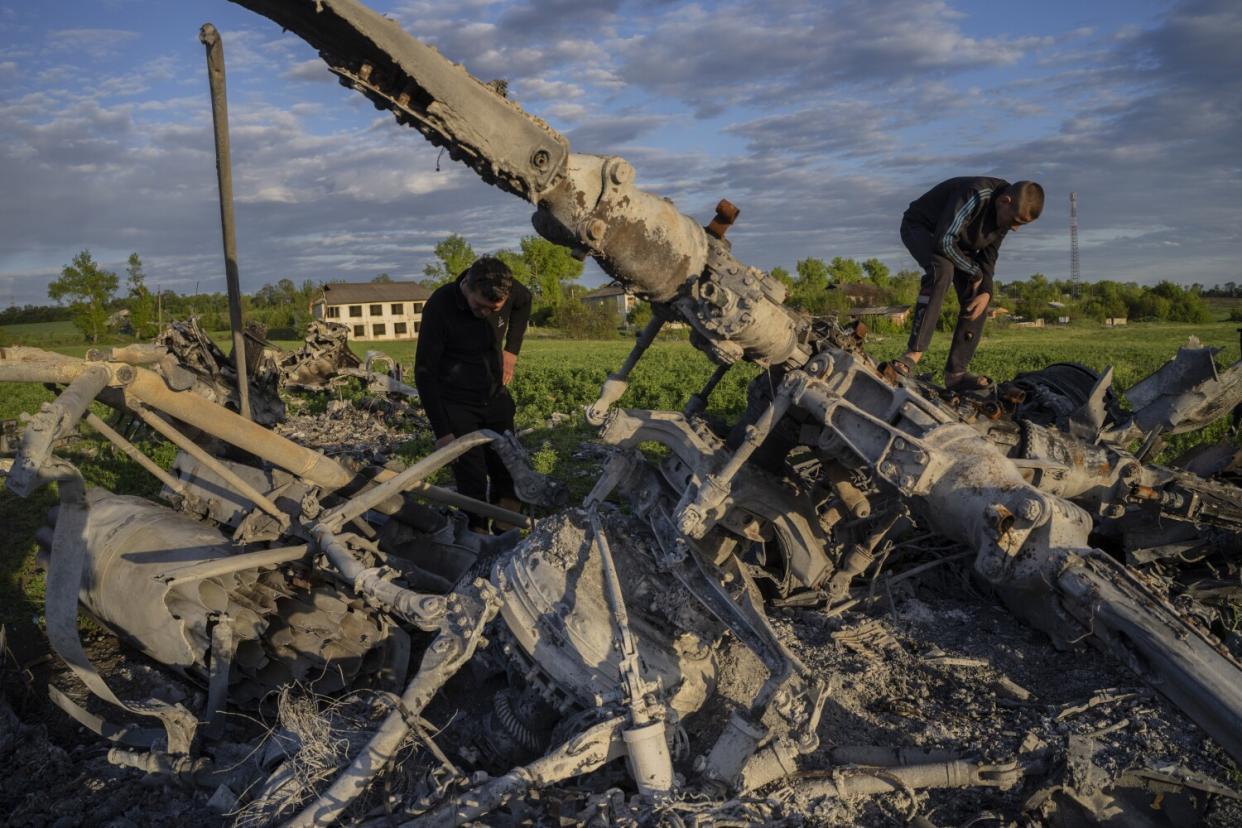 Two men look over the remains of a destroyed helicopter