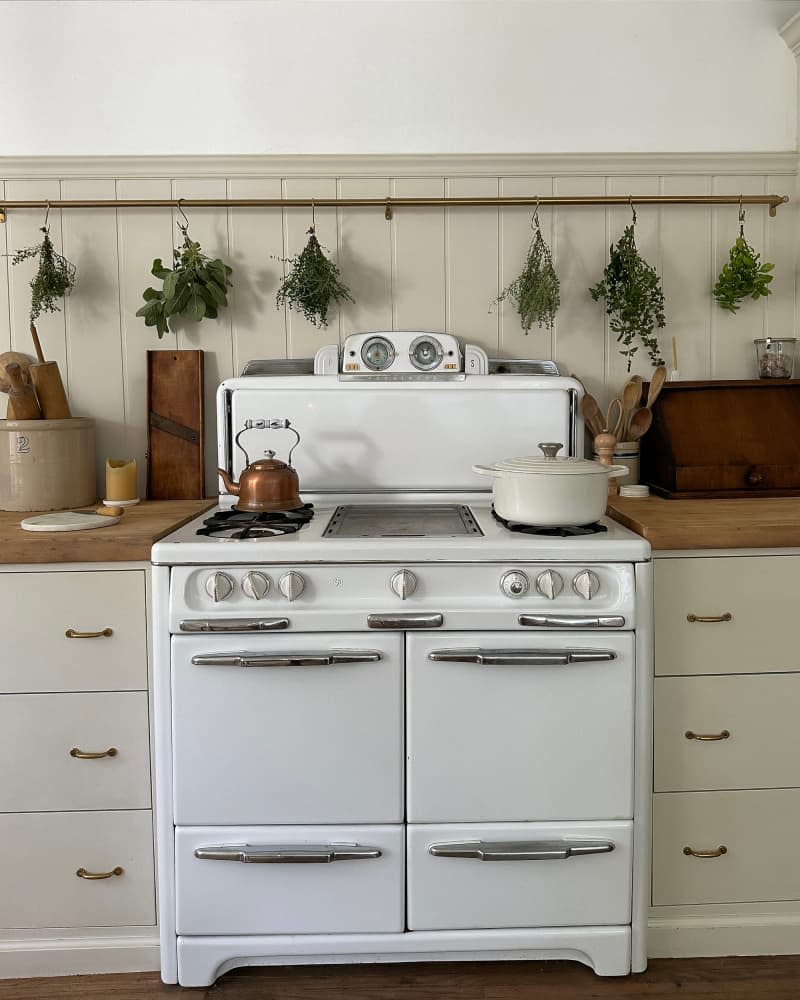 Vintage stove in newly renovated kitchen with herbs drying on brass rail behind.