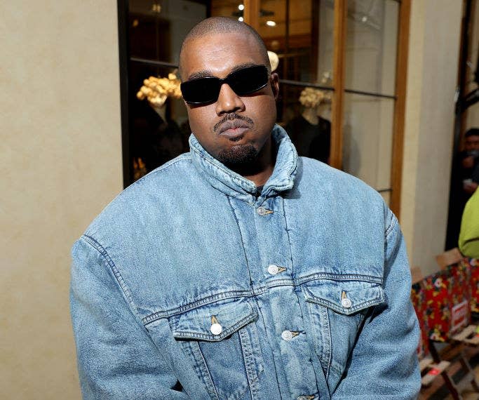 A closeup of Kanye wearing a denim jacket and dark sunglasses