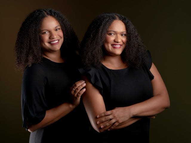 Two women with afros wearing black shirts smile to the camera