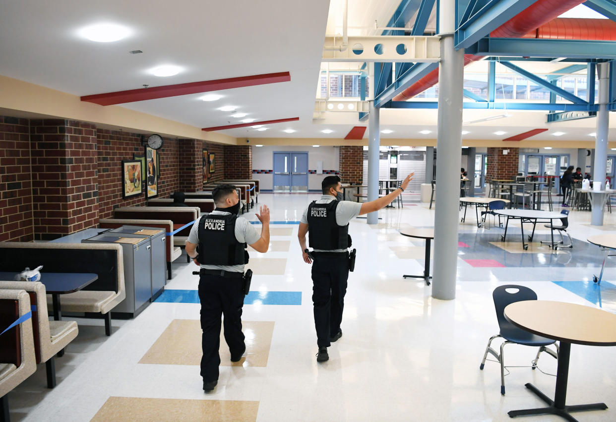 Alexandria Police Department school resource officers wave to students as they walk through the cafeteria