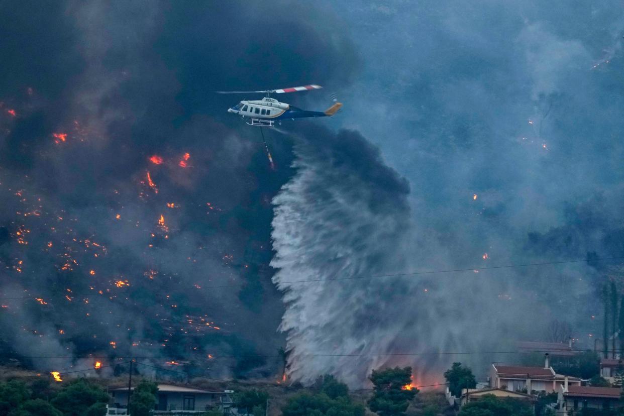 A firefighting helicopter dumps water as fire approach houses in Kalamaki near Agioi Theodori about 60 Kilometres west of Athens (AP)