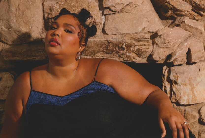 A Black woman with two hair buns poses for pictures in a blue thin-strapped dress.