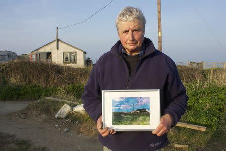 Bryony Nierop-Reading, a 69-year-old pensioner, stands in front of the remains of her home in Happisburgh, while holding a picture of the bungalow before it was demolished after a winter storm left it perched on the edge of a cliff, March 12, 2014. REUTERS/Alister Doyle