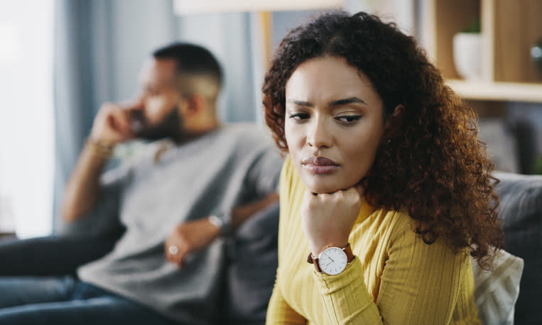 Woman looking sad while her boyfriend sits behind her on the couch