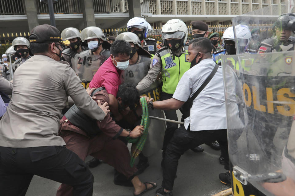 Supporters of Rizieq Shihab, leader of the Islam Defenders Front, scuffle with police officers during a rally in Jakarta, Indonesia, Friday, Dec. 18, 2020. Hundreds of protesters marched in Indonesia's capital on Friday to demand the release of the firebrand cleric who is in police custody on accusation of inciting people to breach pandemic restrictions and ignoring measures to curb the spread of COVID-19 by holding several events, and justice for his six followers who were killed in a shootout with the police. (AP Photo/Tatan Syuflana)