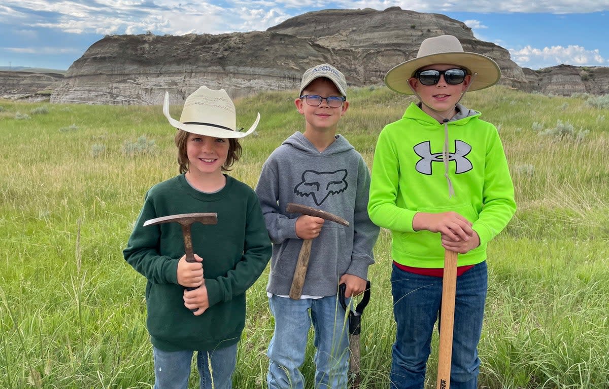 In this image provided by Giant Screen Films, Liam Fisher, Kaiden Madsen and Jessin Fisher pose for a celebratory photo on the day their fossil find was determined to be a juvenile T rex, in North Dakota (David Clark/Giant Screen Films via AP)