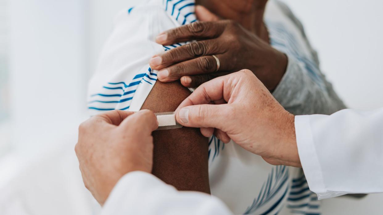  Close up on an older woman's arm as male doctor places a bandage on it, as if she's just received a vaccine. 